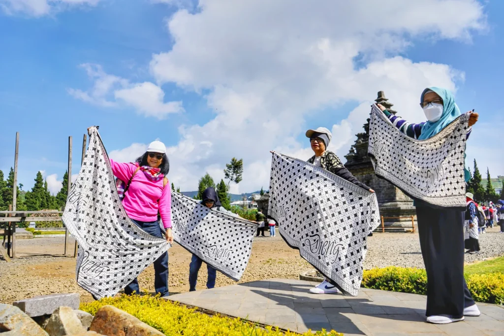Tourists displaying traditional batik near a temple in Dieng Plateau, Central Java.