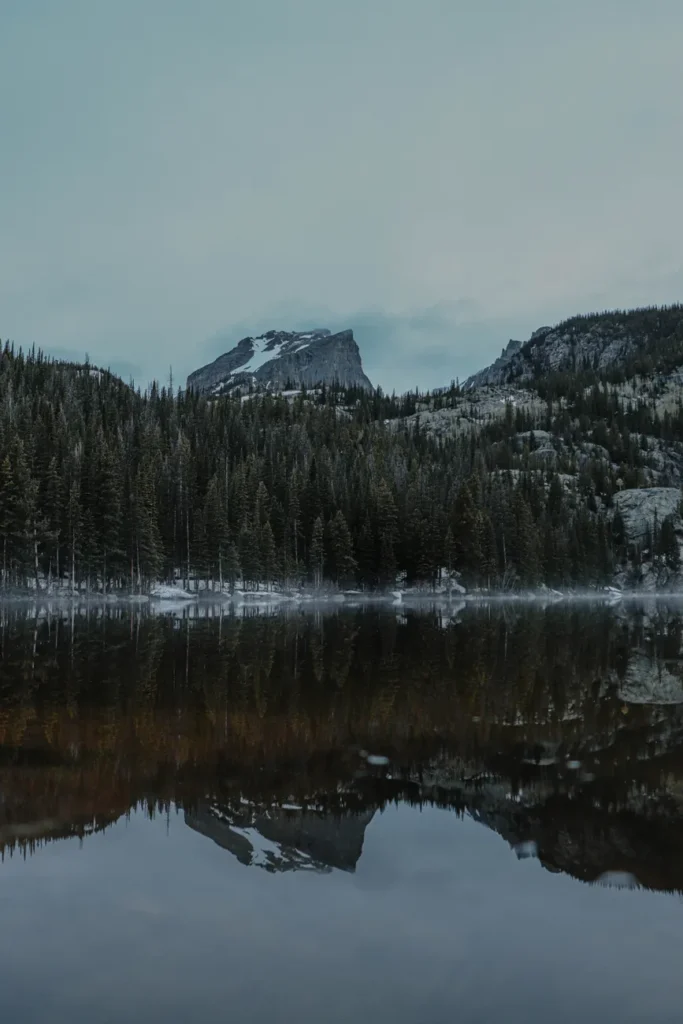 Tranquil scene of snowcapped mountains reflecting in a forest lake in Estes Park, Colorado.