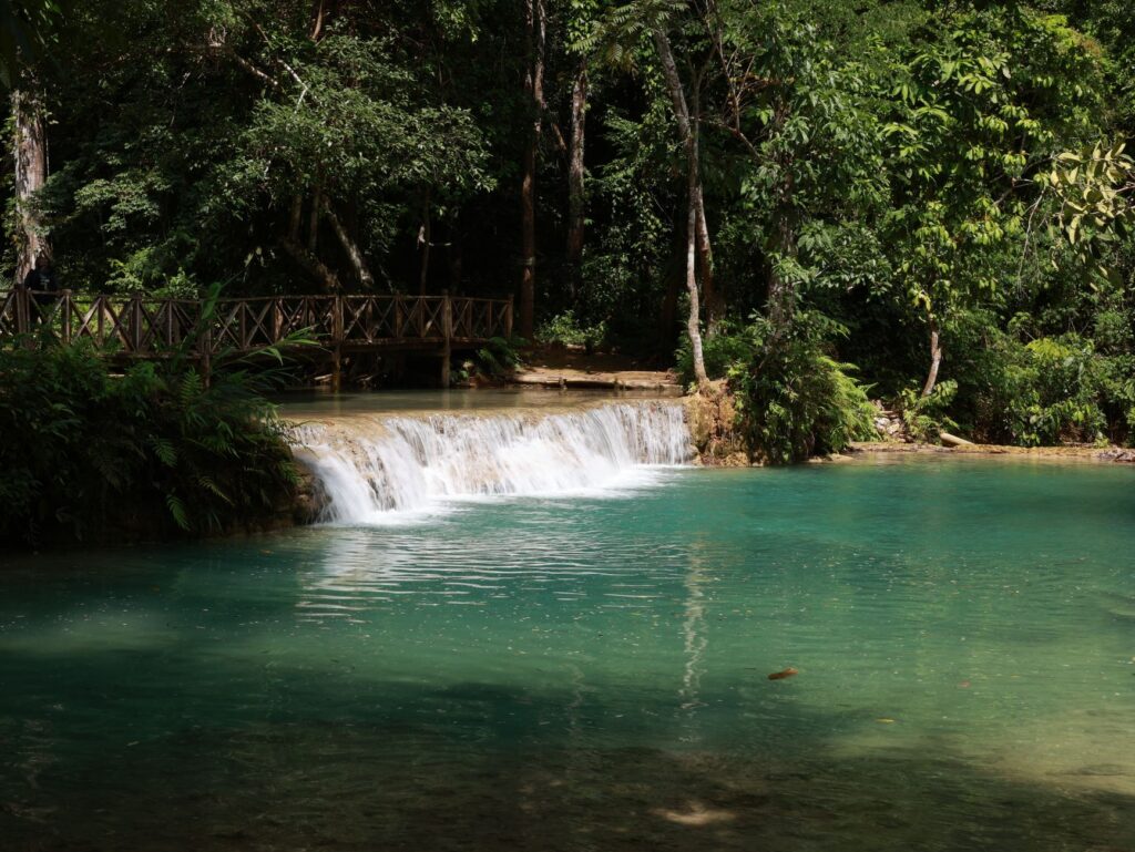Tranquil turquoise waters cascading at Kuang Si Waterfall in a lush forest setting, Luang Prabang, Laos.