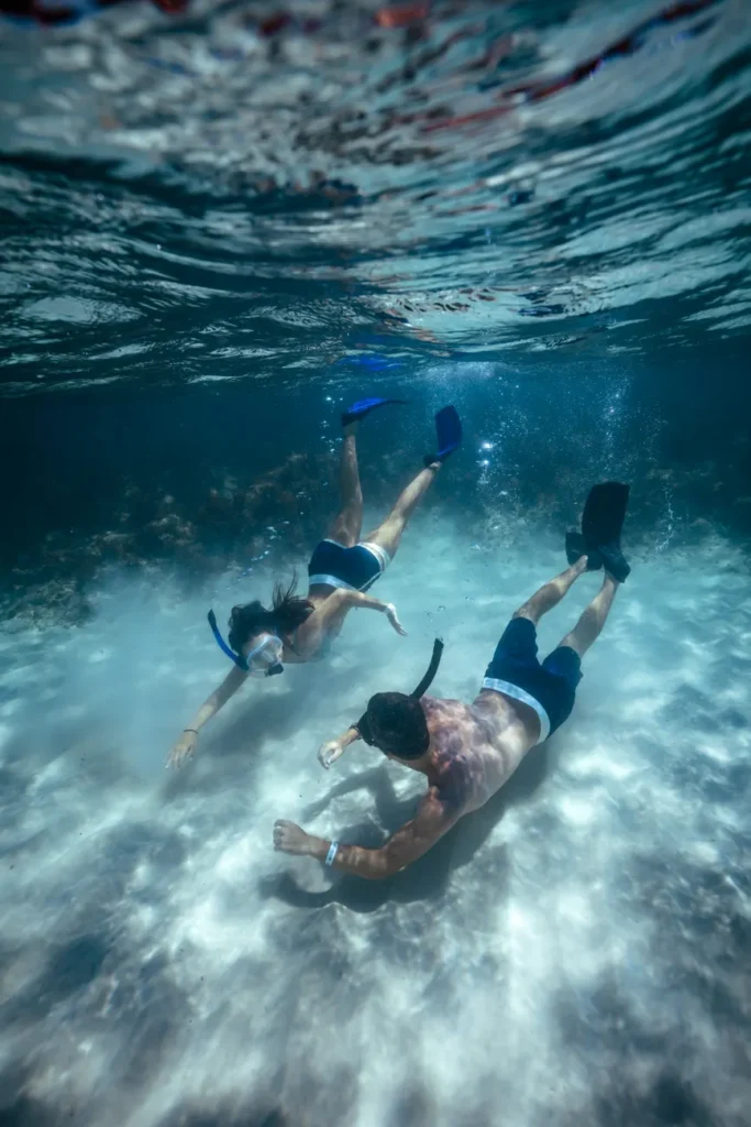Two adults snorkeling underwater, exploring coral reefs in clear ocean waters.