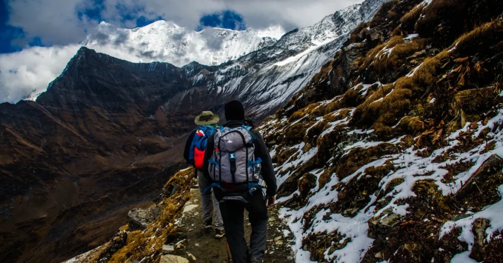 Trek EBC : la journée 3 entre Namche Bazaar et les hôtels d’altitude (mode couple, sans prise de tête) Two hikers navigating a snowy trail in rugged mountainous terrain under dramatic skies.