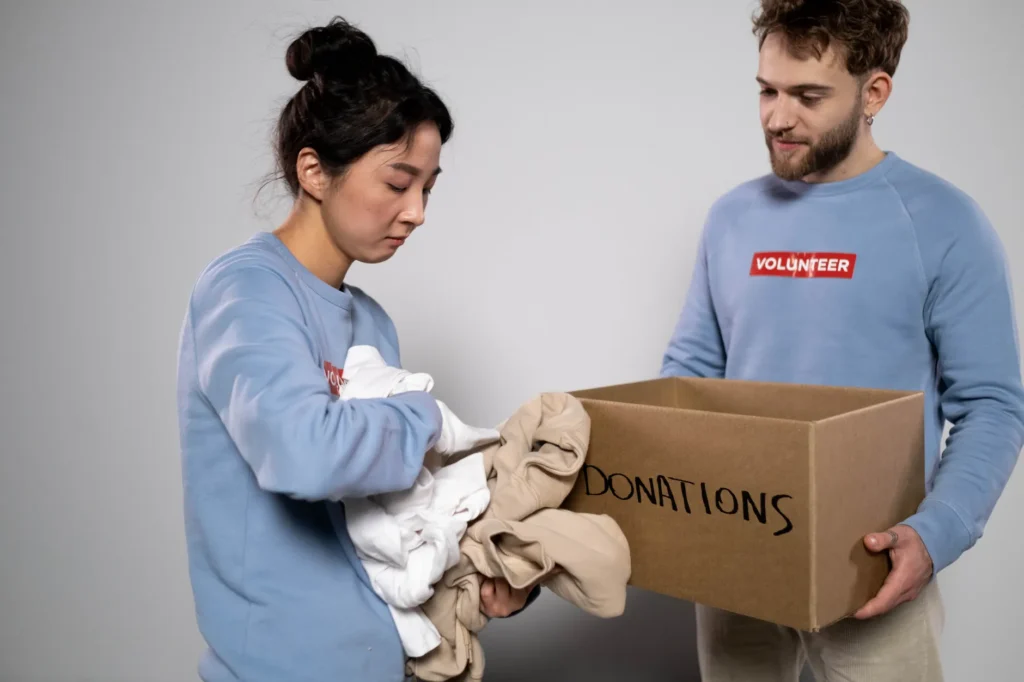 Two volunteers organizing clothes into a donation box, showcasing community service and generosity.
