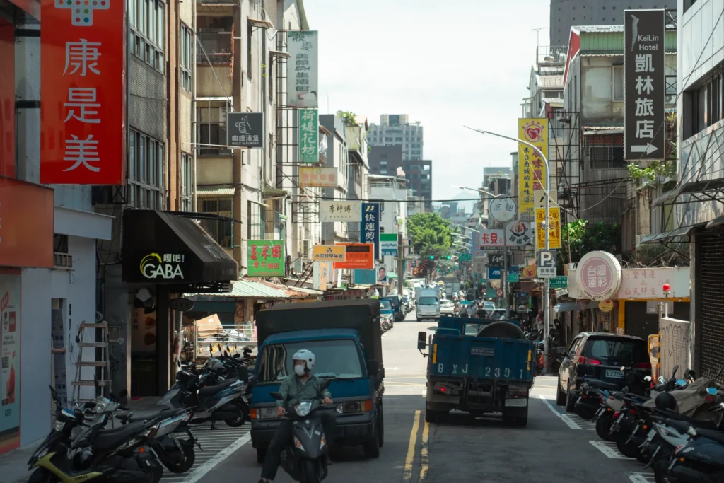 Vibrant Taipei street scene with scooters and cars amidst colorful shop signs.