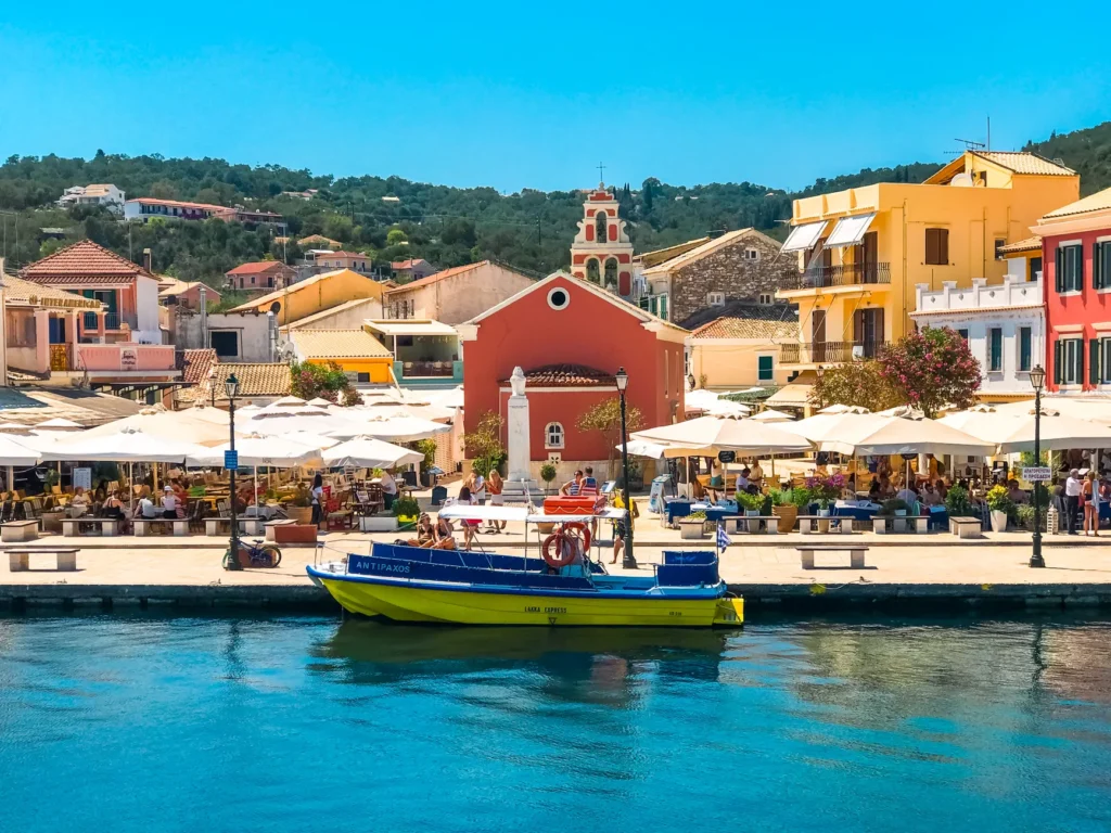 Vibrant waterfront in Fiskardo, Greece with boat, café, and colorful buildings on a sunny day.