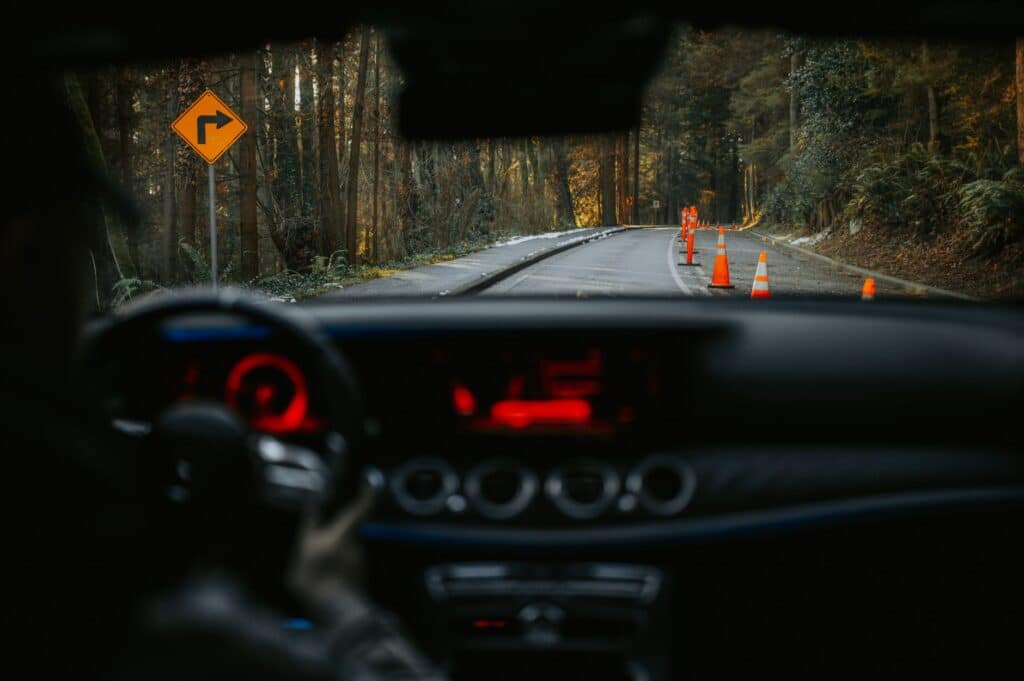 View from car dashboard of rural road with traffic cones and turn sign. Scenic forest driving experience.