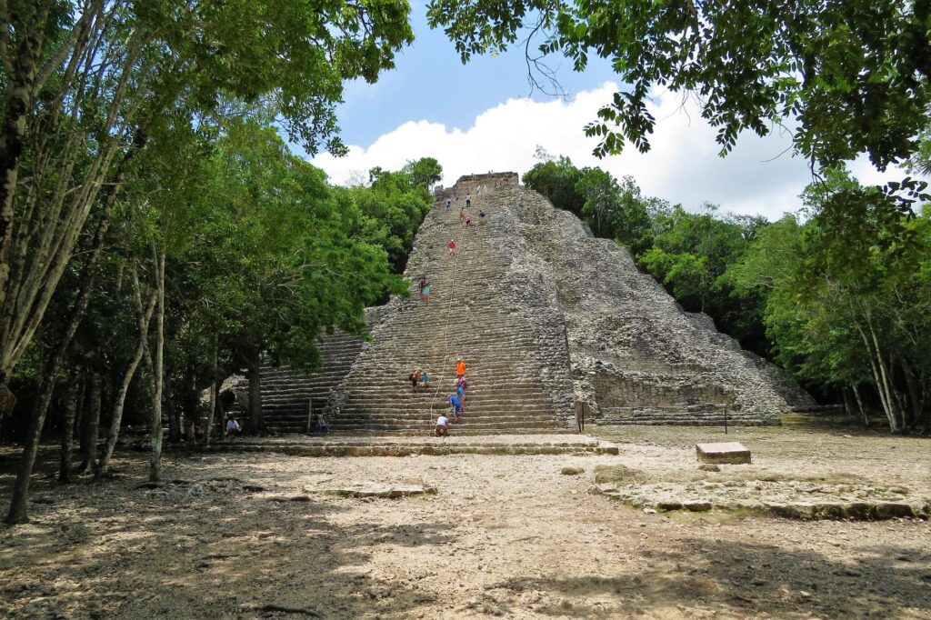 Visitors climbing the ancient Coba Mayan pyramid surrounded by lush jungle in Mexico.