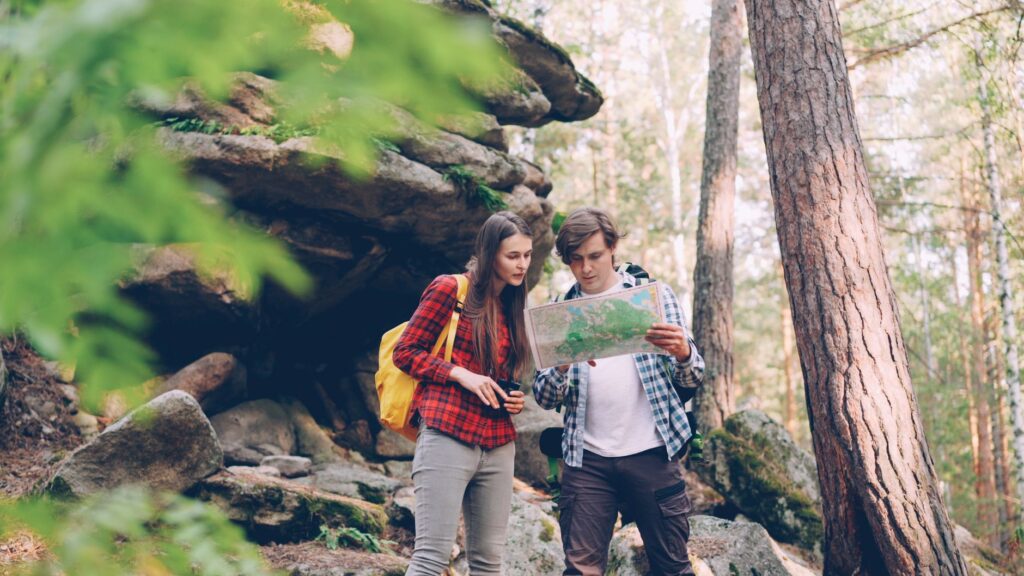 Young couple hiking in forest, using map for navigation. Adventure and nature concept.