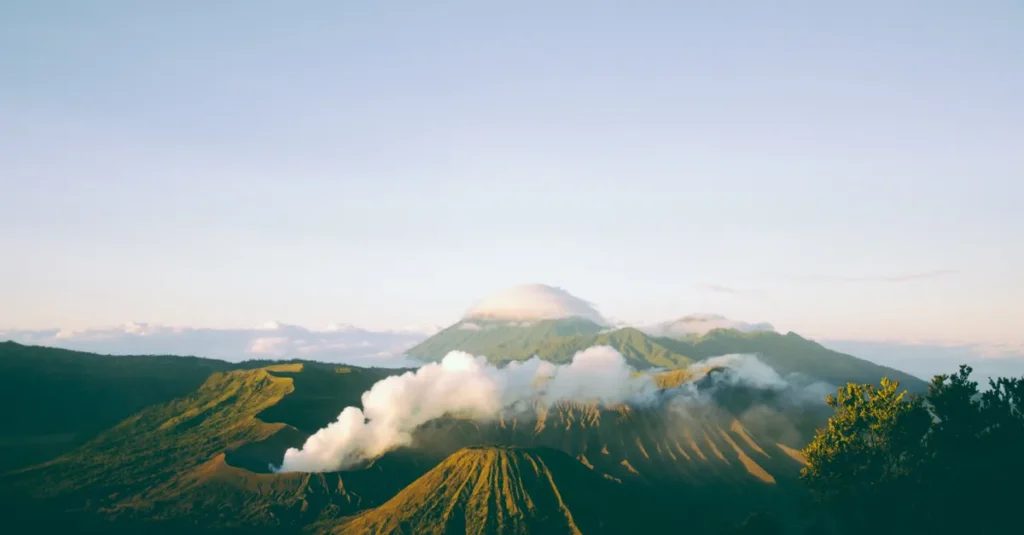 Java à deux en 7 jours : temples, cascades et volcans (rythme malin + pièges à éviter) A breathtaking view of Mount Bromo emitting smoke at sunrise, surrounded by lush landscapes of East Java, Indonesia.