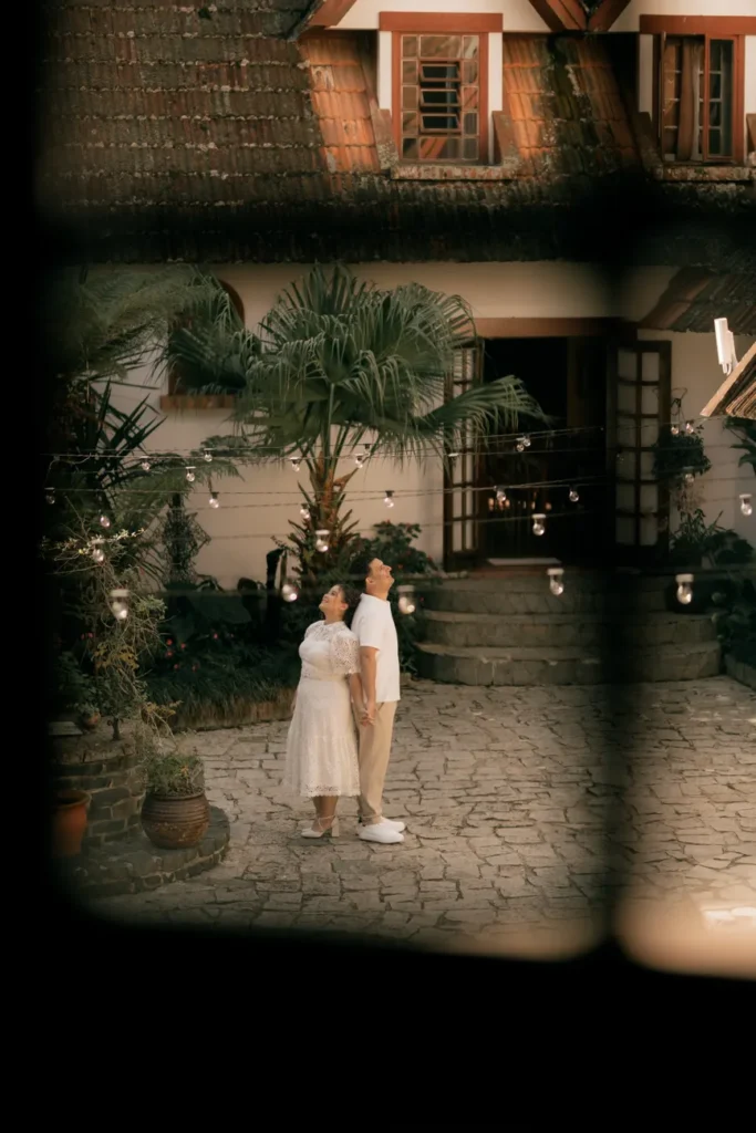 A couple enjoying a serene moment in a picturesque courtyard with plants and hanging lights.