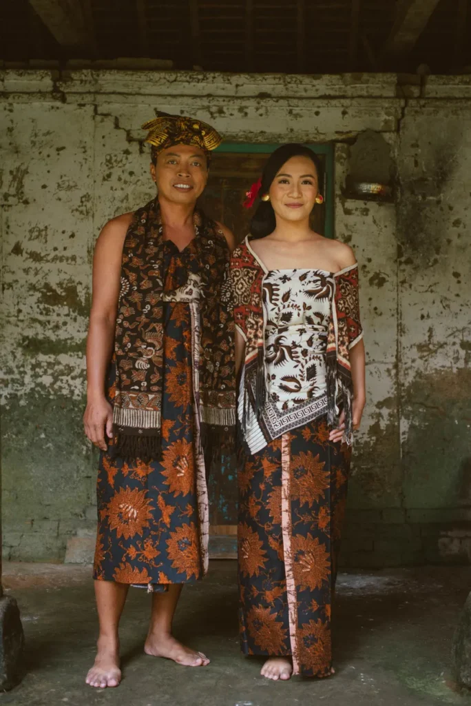 A couple in traditional Balinese clothing standing indoors, showcasing cultural heritage.