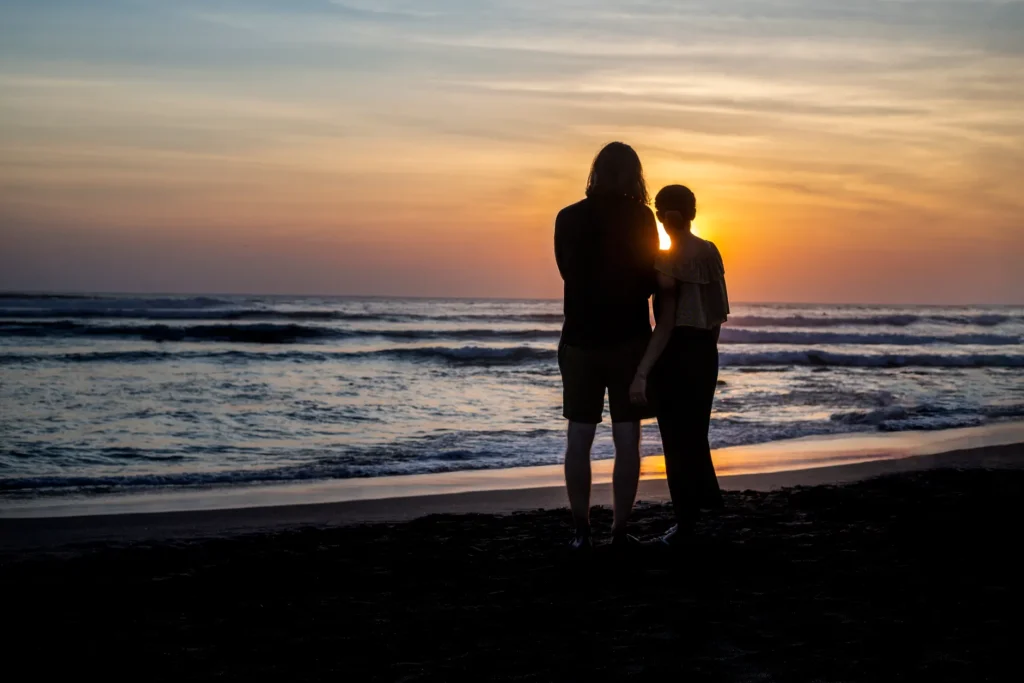 A couple stands on a Bali beach at sunset, creating a romantic silhouette against the ocean view.