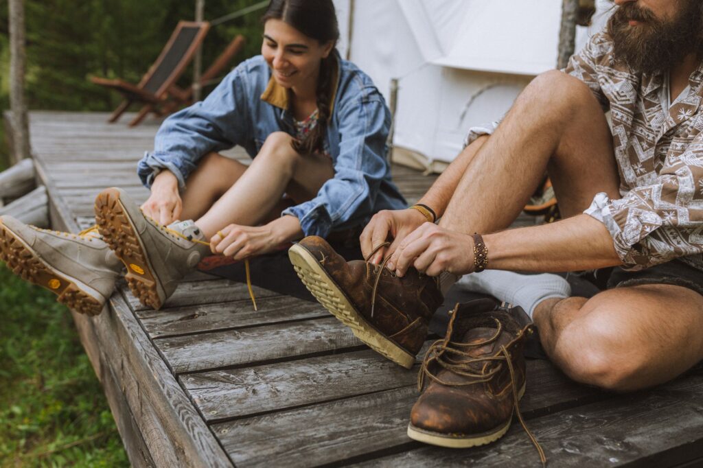 A couple ties their hiking boots on a wooden deck, enjoying a sunny day outdoors.
