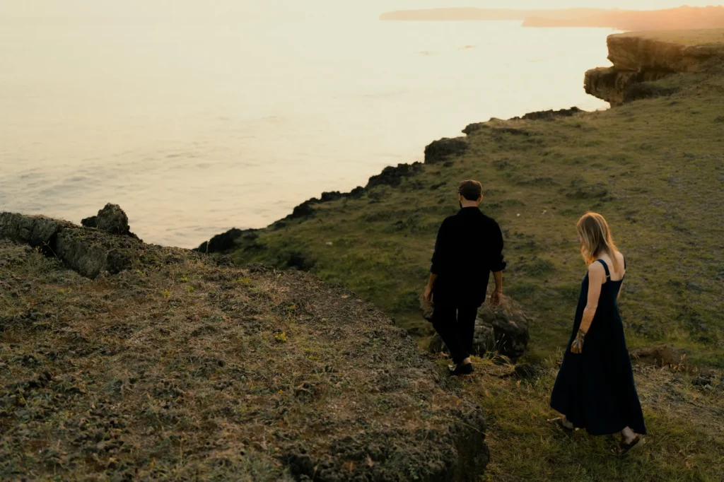 A couple walks along a scenic cliff with the ocean backdrop during a tranquil sunset.