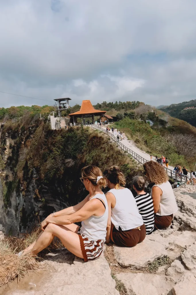 A group of tourists sitting on the edge of a cliff at Angel's Billabong, Nusa Penida, Indonesia