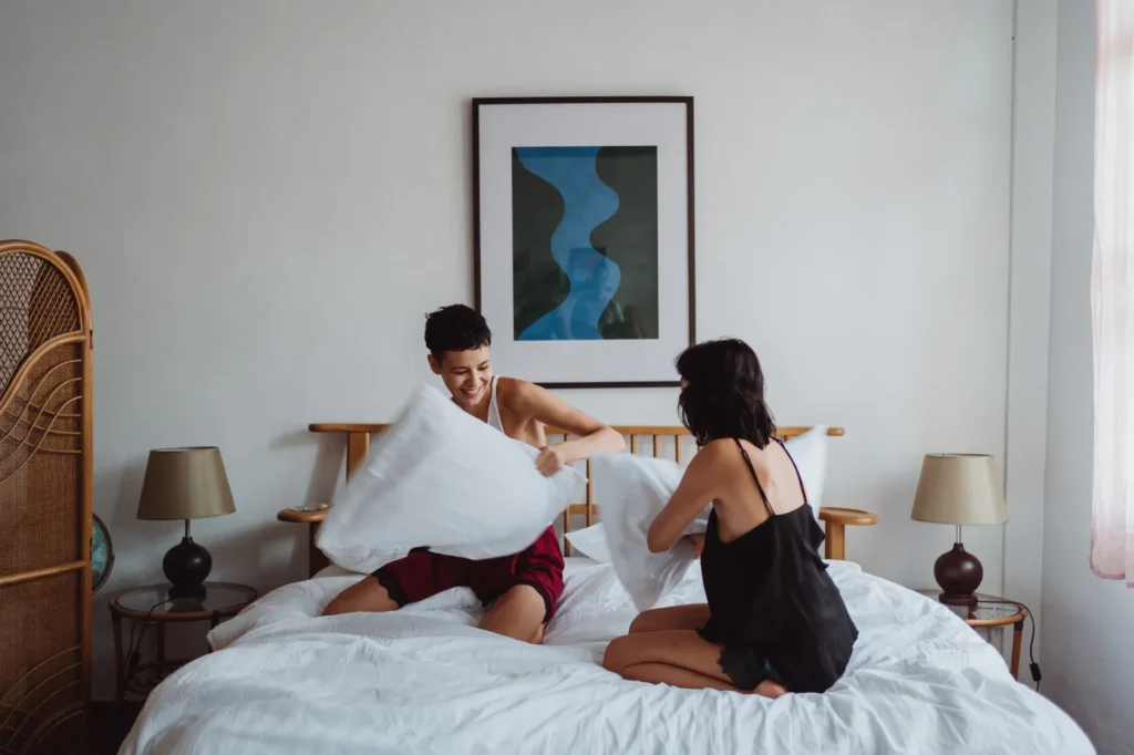 A happy couple enjoying a playful pillow fight in a modern bedroom setting.