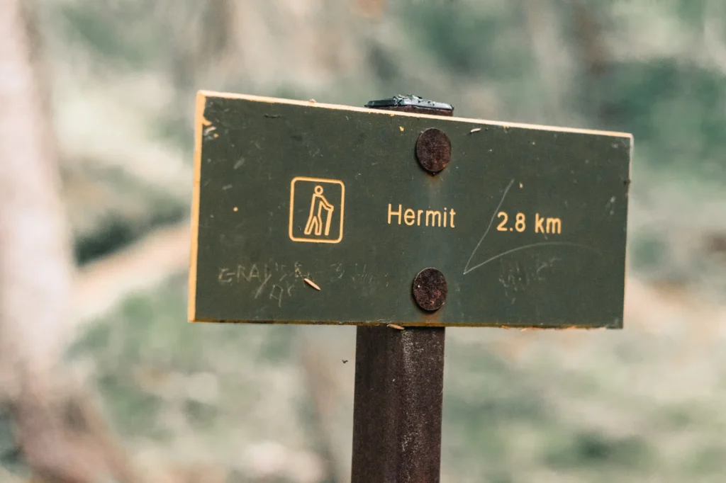 A hiking trail sign pointing to Hermit, located 2.8 km away in a forest setting.