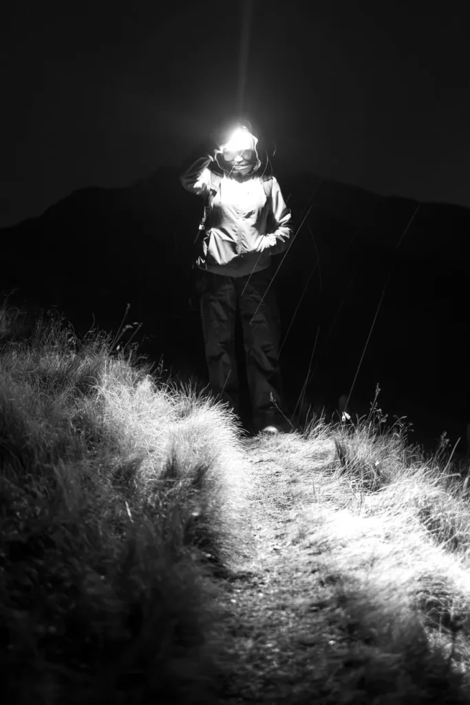 A lone hiker illuminates a dark trail with a headlamp, creating a mysterious and adventurous atmosphere.