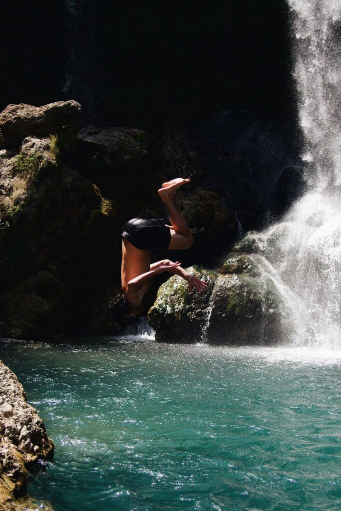 A man dives into a turquoise pool near a waterfall, showcasing adventure and nature.