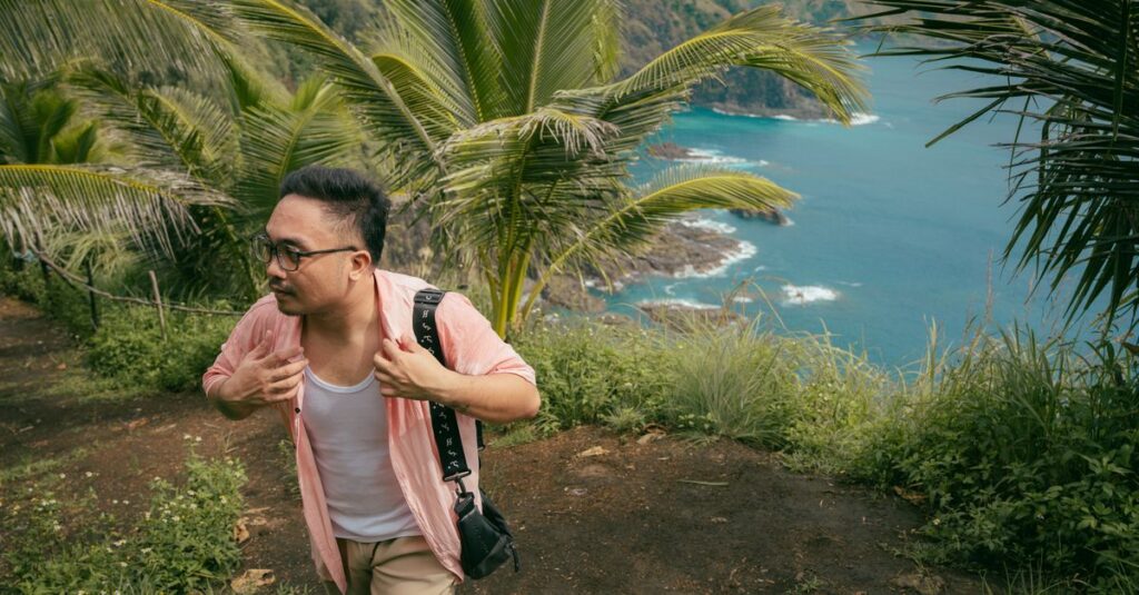 Crouching Lion Hike à Oʻahu à deux : la rando courte qui fait vraiment le job (sans cardio inutile) A man hiking a lush tropical trail with ocean views and palm trees, depicting outdoor adventure.