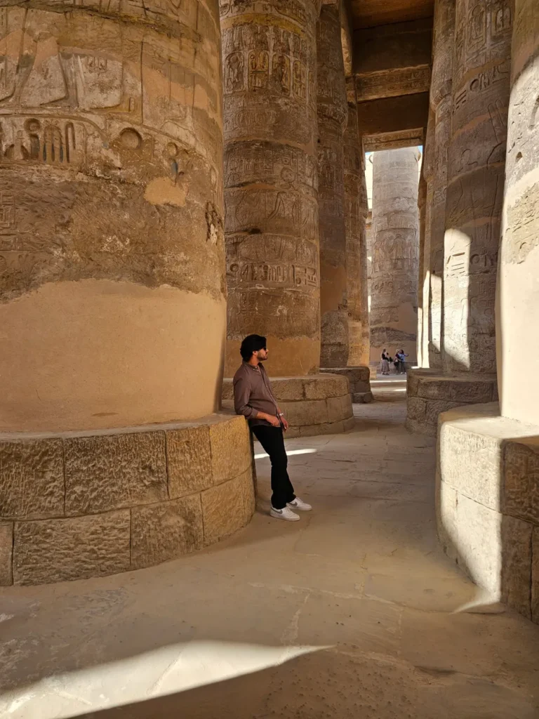 A man leans on a large column in the historic Karnak Temple complex in Luxor, Egypt.
