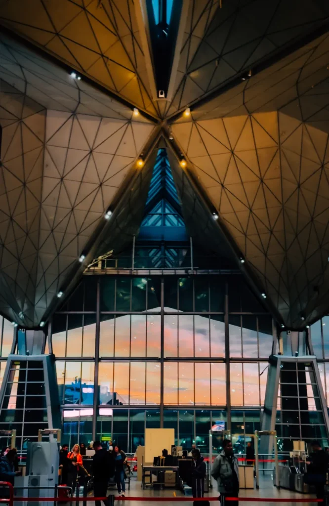 A modern airport terminal with stunning architectural design illuminated at sunset, depicting a busy scene with travelers.