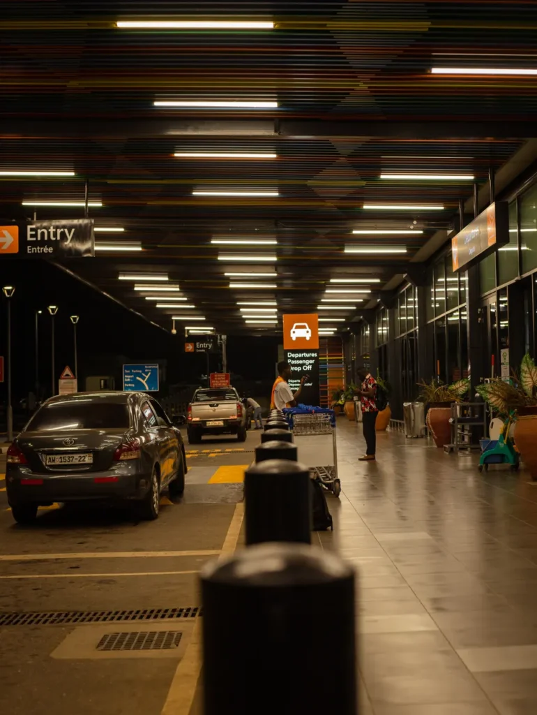 A nighttime view of an airport drop-off zone featuring parked cars and passengers.