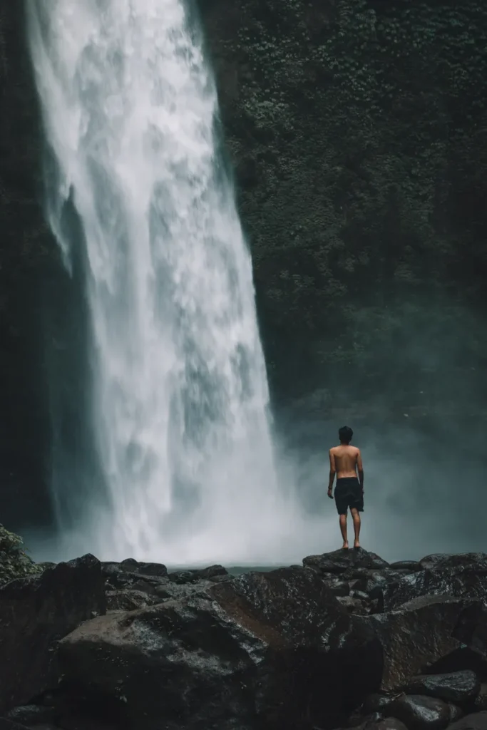 A person stands before a majestic waterfall in Ubud, Bali, capturing the essence of adventure and nature.