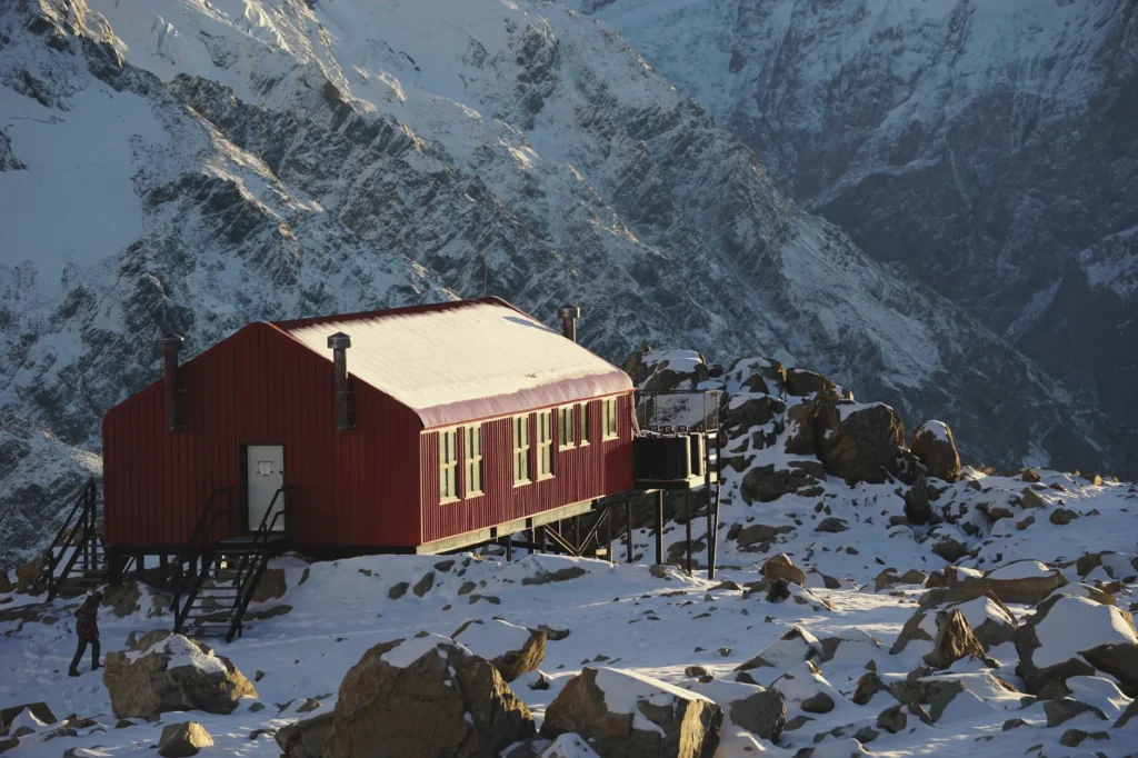 A red alpine hut stands against snowcapped mountains in Mount Cook National Park, New Zealand.