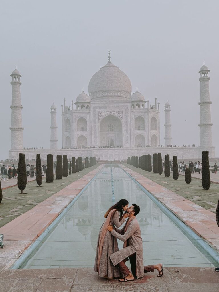A romantic couple kissing in front of the iconic Taj Mahal in Agra, India.
