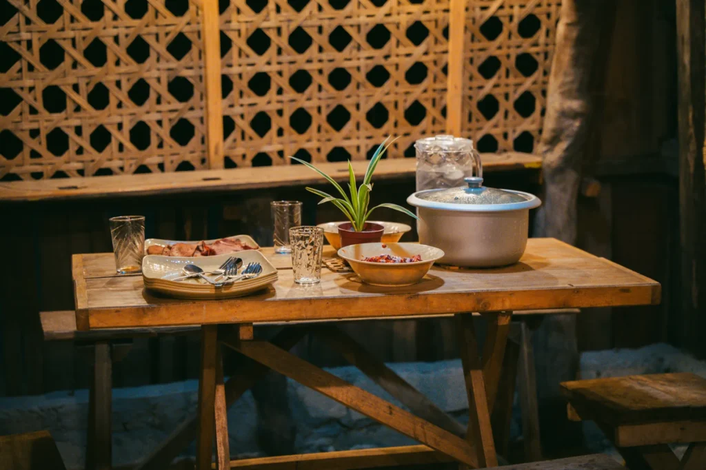 A rustic dining table set with plates, bowls, and a potted plant, creating a cozy indoor atmosphere.