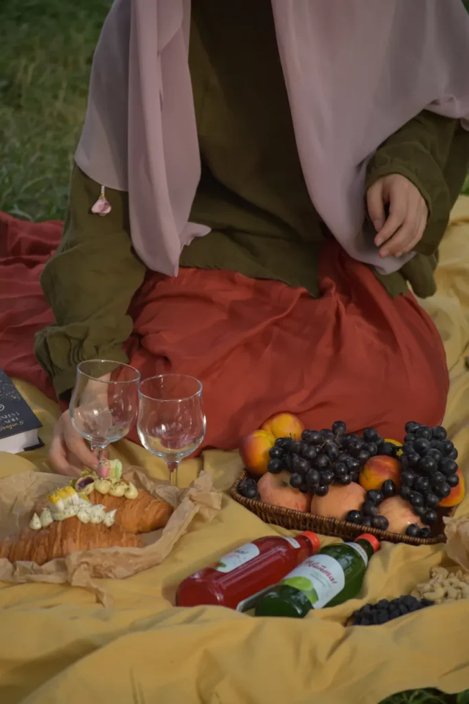 A serene picnic setup with fruits, pastries, and drinks on a blanket outdoors.