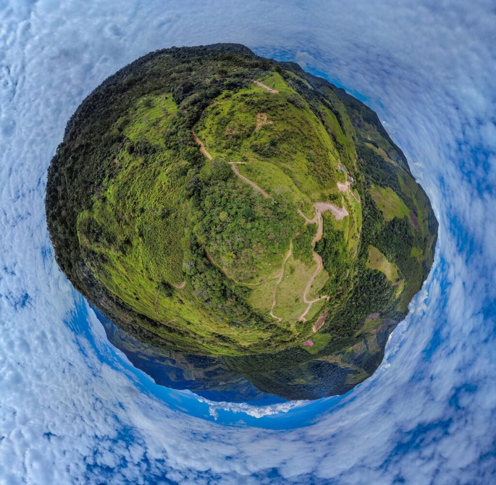 A stunning 360-degree view of lush green hills forming a tiny planet effect under a bright sky.