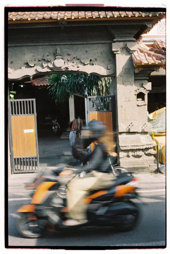 A vibrant street shot capturing a scooter zooming past traditional Balinese architecture.