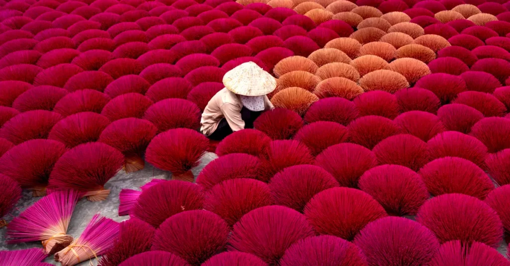 Quang Phu Cau à deux : le village d’encens près de Hanoï, guide concret (sans pièges) A Vietnamese worker in Quang Phu Cau crafting incense sticks outdoors, surrounded by vibrant colors.