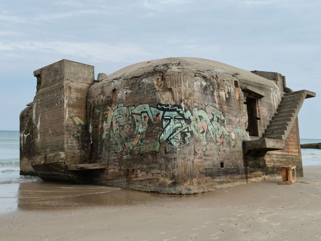A weathered, graffiti-covered bunker sits on the sandy beach of Løkken, Denmark.