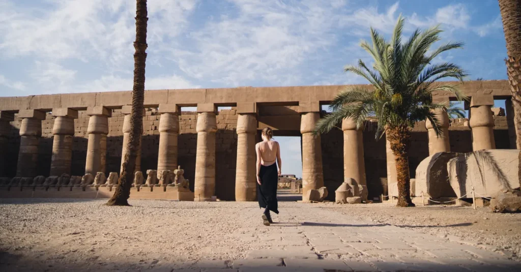 Visiter Karnak à deux à Louxor : le guide concret (rythme, spots, pièges) A woman in a backless black dress walking at the historic Karnak Temple in Egypt.
