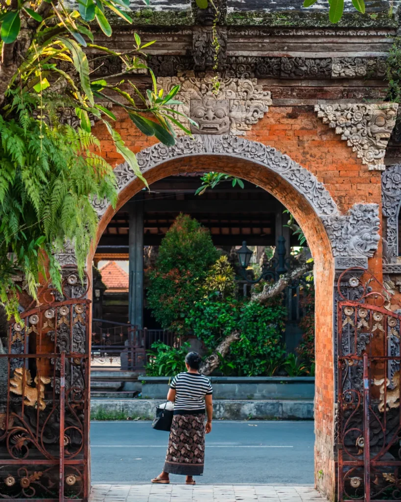 A woman in traditional attire stands at the ornate entrance of a Balinese temple in Ubud, Indonesia.