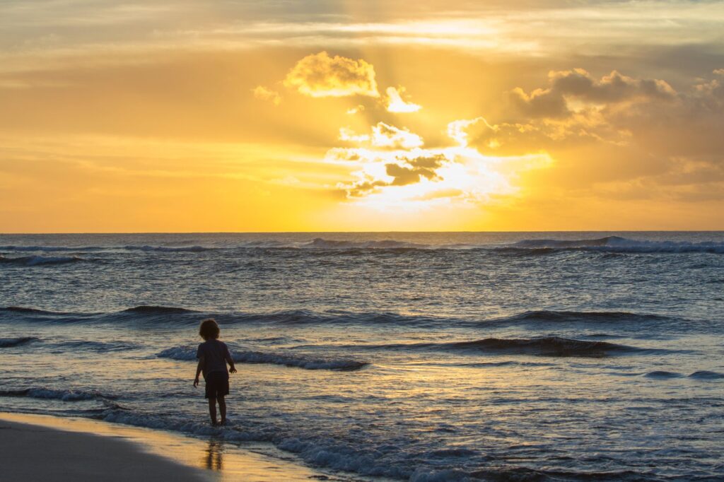 A young child enjoying the sunset on the beach in Haleiwa, Hawaii, with golden hour light reflecting on the ocean.