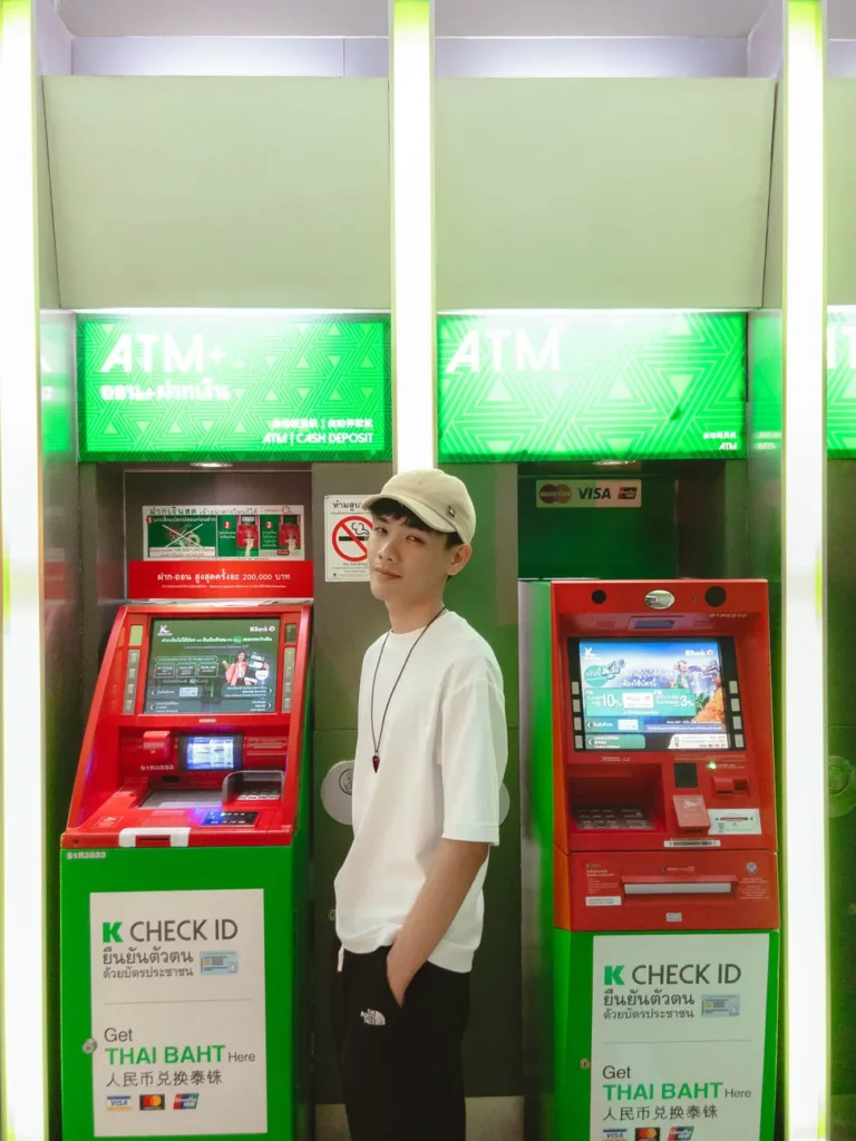 A young man standing between two ATMs, wearing casual attire, indoors.