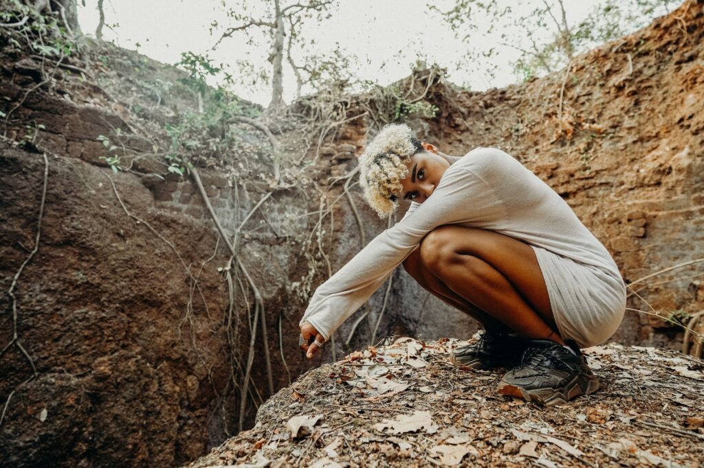 A young woman with curly hair crouches on the edge of a canyon in a national park.