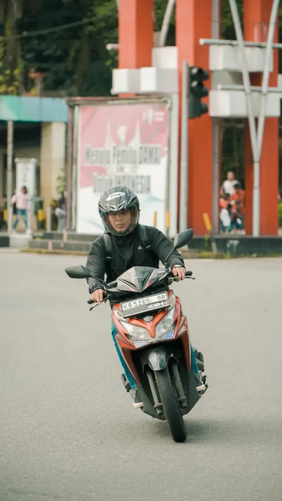 Adult man wearing a helmet rides a motor scooter through a city intersection, capturing urban commuting.
