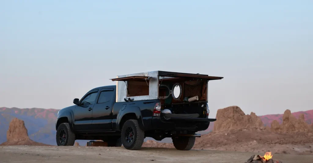 Road trip à deux en truck tent : dormir dans une benne au-dessus du sol (Colorado, Utah, Zion) Adventure scene of an off-road pickup truck camping in a desert landscape with a small bonfire.