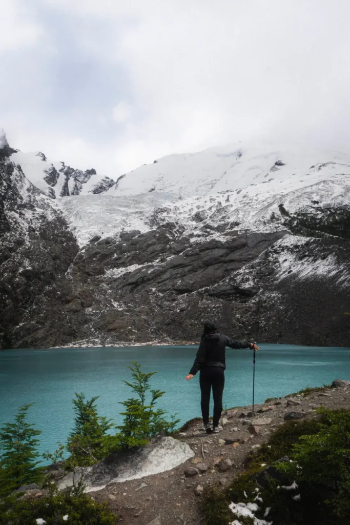 Adventurer views snow-capped mountains and turquoise lake in Patagonia.
