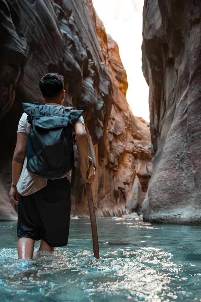 Adventurer wading through water in Zion's iconic canyon setting, capturing nature's rugged beauty.
