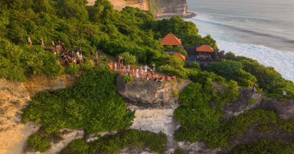 Batu Jaran Hill à deux : le sunset à Uluwatu sans foule (et avec la bonne prudence) Aerial view of Uluwatu Cliffs in Bali with lush greenery and a gathering of people enjoying the sunset.
