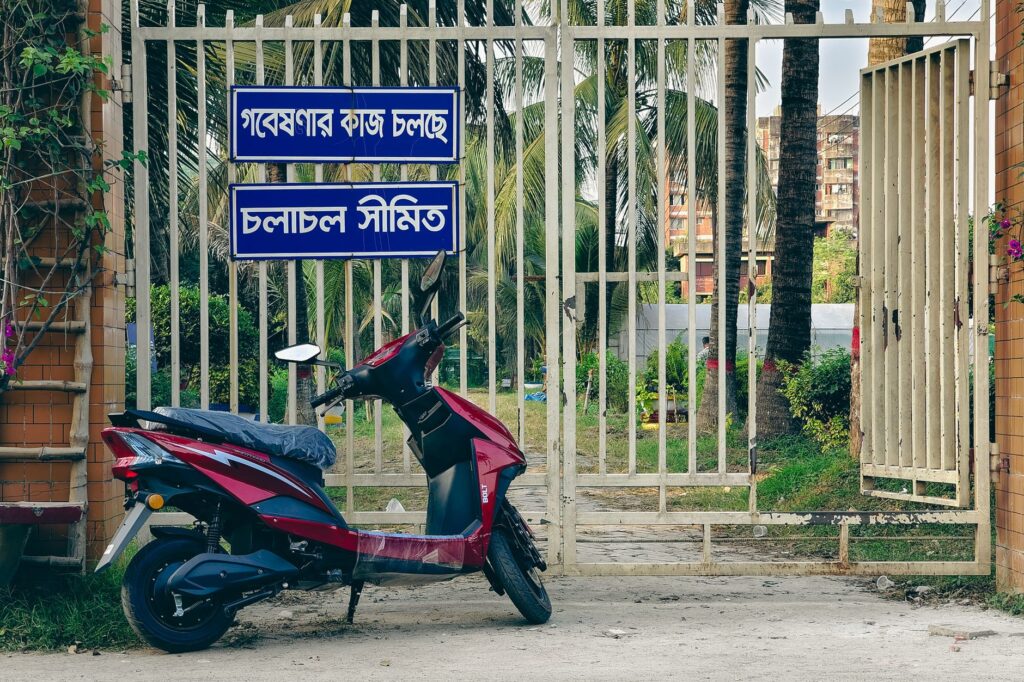 An electric scooter parked near a gated entrance with palm trees in the background, suggesting tranquility and urban lifestyle.