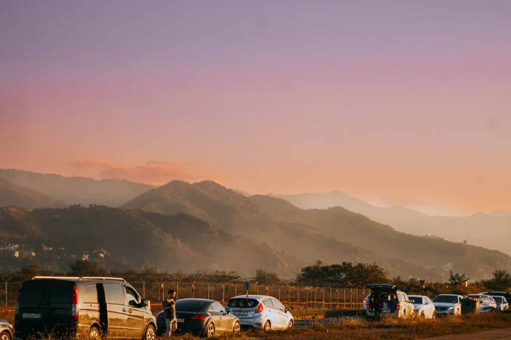 Beautiful sunset landscape in Batumi, Georgia, with parked cars and misty mountains in the background.