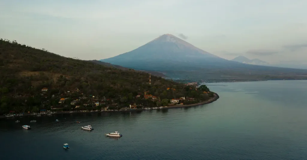 Sanur à Bali en couple : le guide concret “calme, lever de soleil & plan sans galère” Breathtaking aerial shot of Bali's Mount Agung with tranquil coastal waters at sunrise.