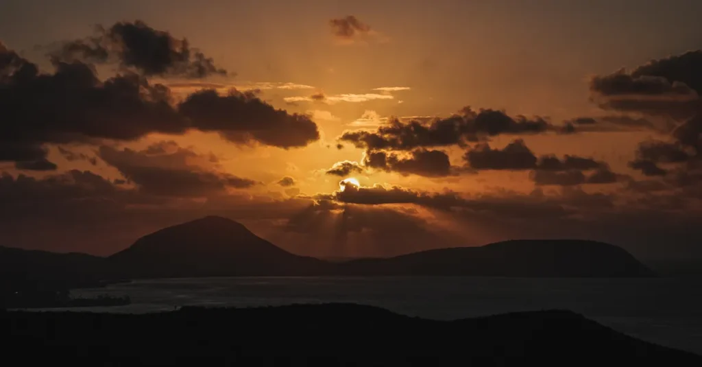 Ka’ena Point à deux (O‘ahu) : le sunset parfait, sans se cramer ni se perdre Breathtaking Hawaiian sunset over silhouettes of mountains and ocean, captured during golden hour.