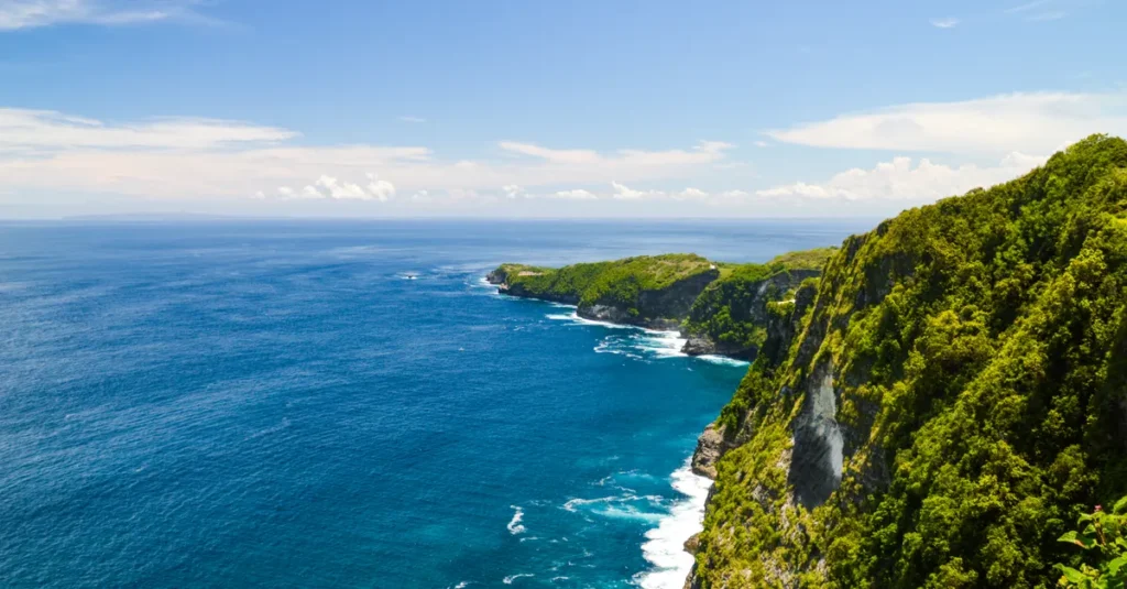 Paluang Cliff à Nusa Penida en couple : la vue canon (et le plan sans se cramer) Breathtaking view of lush cliffs meeting blue ocean waters in Bali, Indonesia.
